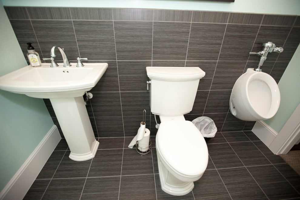 Klassisk inredning av ett litet toalett, med ett urinoar, brun kakel, keramikplattor, gröna väggar, klinkergolv i keramik, ett piedestal handfat och brunt golv