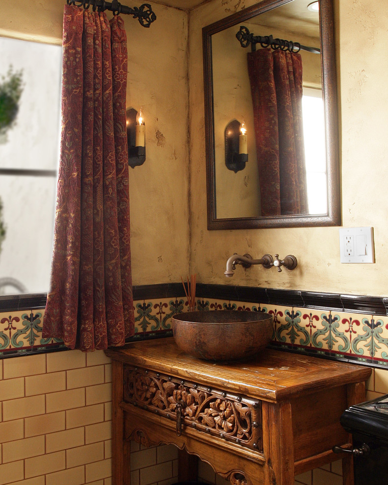 Small mediterranean cloakroom in Los Angeles with freestanding cabinets, medium wood cabinets, a two-piece toilet, multi-coloured tiles, ceramic tiles, a vessel sink, wooden worktops, beige walls and brown worktops.