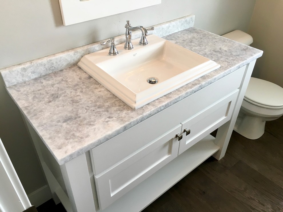 Immagine di un bagno di servizio american style con piastrelle grigie, pareti grigie, pavimento in vinile, lavabo integrato, top in granito e ante bianche