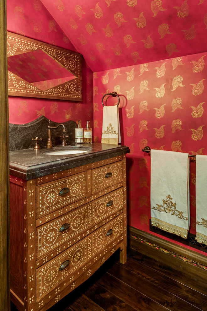 Asiatische Gästetoilette mit verzierten Schränken, hellbraunen Holzschränken, roter Wandfarbe, dunklem Holzboden, Unterbauwaschbecken, braunem Boden und schwarzer Waschtischplatte in Providence