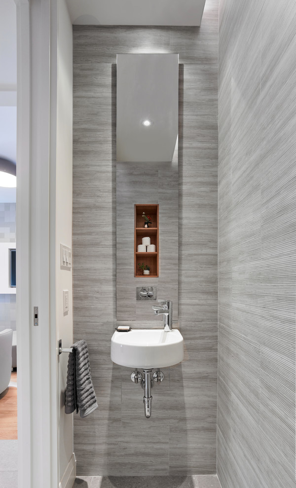 Bild på ett litet funkis toalett, med grå kakel, ett väggmonterat handfat, grått golv och vita väggar