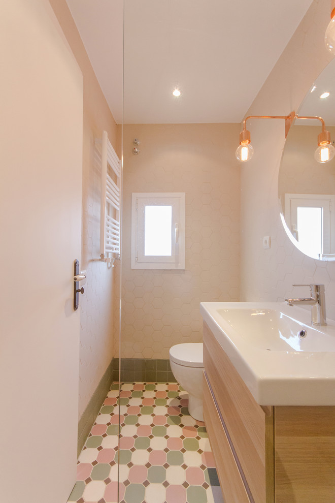 Réalisation d'un WC et toilettes design en bois clair de taille moyenne avec un placard à porte plane, WC à poser, des carreaux de céramique, un mur beige, un sol en carrelage de céramique et un lavabo intégré.