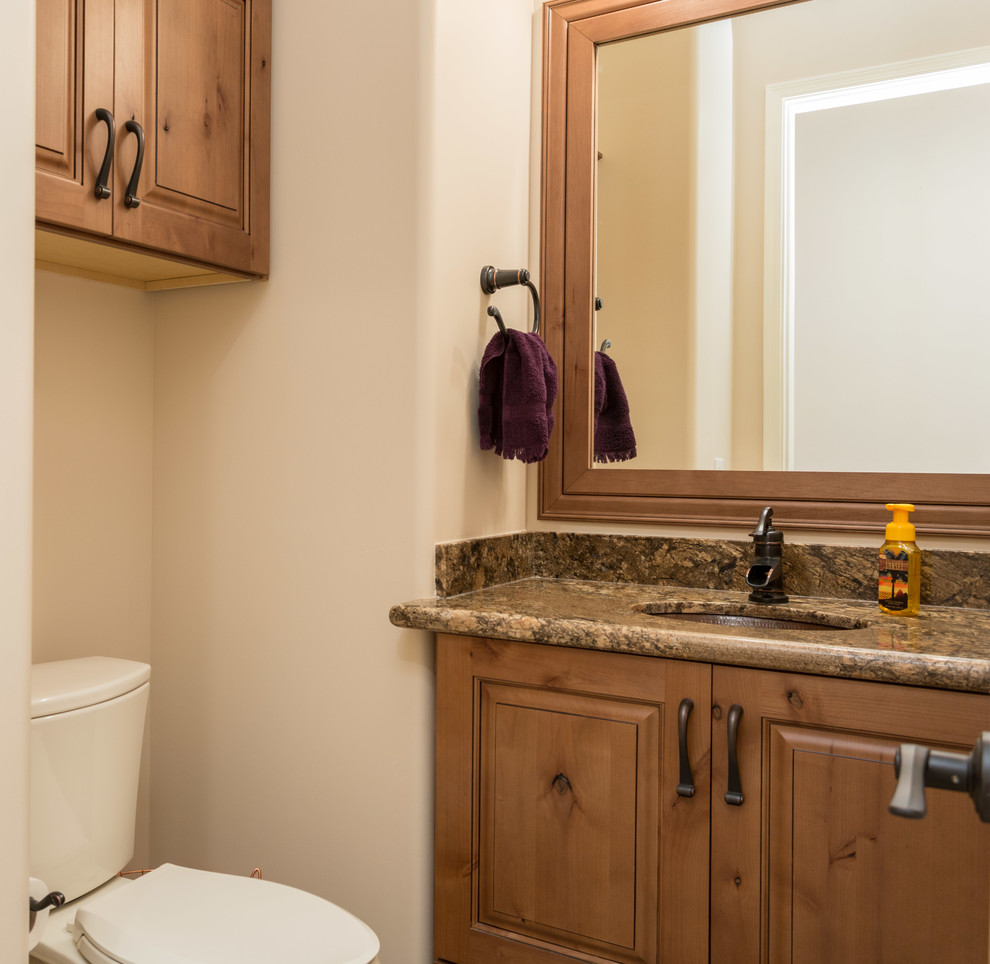 Bild på ett litet rustikt toalett, med ett nedsänkt handfat, skåp i mellenmörkt trä, granitbänkskiva, en toalettstol med hel cisternkåpa, beige väggar och luckor med upphöjd panel