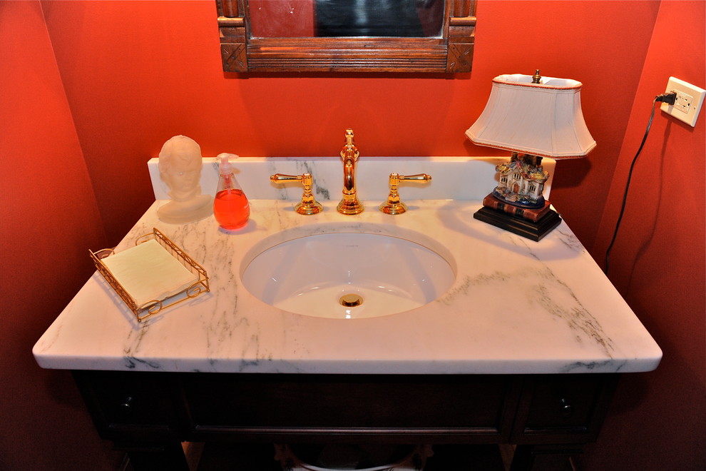 Cette image montre un WC et toilettes traditionnel en bois foncé de taille moyenne avec un placard en trompe-l'oeil, WC séparés, un mur rouge, un sol en bois brun, un lavabo encastré et un plan de toilette en marbre.