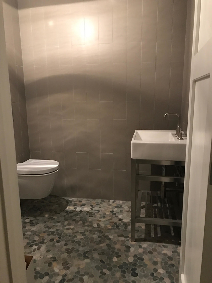 Photo of a medium sized traditional cloakroom in Santa Barbara with open cabinets, a wall mounted toilet, beige tiles, metro tiles, beige walls, pebble tile flooring, a pedestal sink and grey floors.