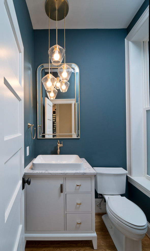 Réalisation d'un WC et toilettes minimaliste avec un placard à porte plane, un mur bleu, un sol en bois brun, une vasque, un plan de toilette en quartz modifié et un plan de toilette blanc.