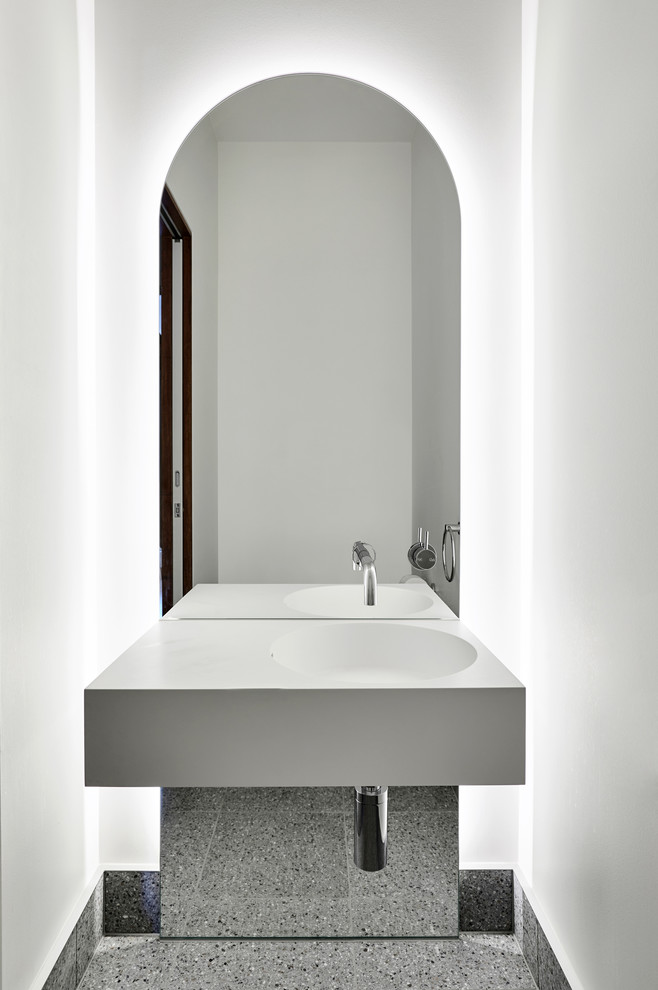 Modern inredning av ett litet vit vitt toalett, med öppna hyllor, vit kakel, vita väggar, betonggolv, ett väggmonterat handfat, bänkskiva i akrylsten och grått golv