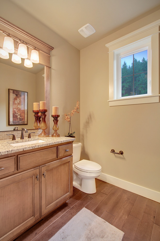 Aménagement d'un WC et toilettes craftsman en bois clair avec un lavabo encastré, un placard avec porte à panneau encastré, un plan de toilette en granite, WC séparés, un carrelage beige, un mur beige et un sol en bois brun.