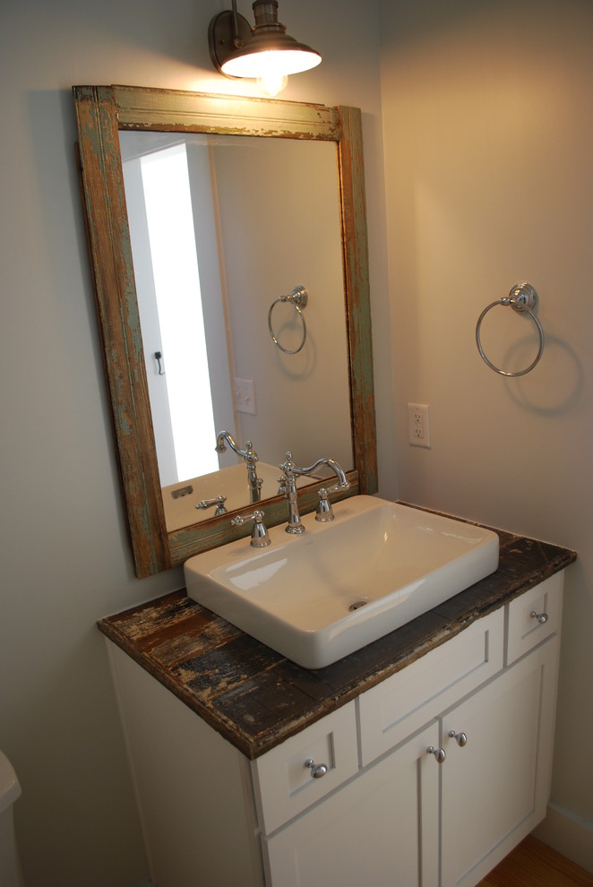 Idée de décoration pour un WC et toilettes champêtre de taille moyenne avec un placard à porte shaker, des portes de placard beiges, un mur beige, un sol en bois brun, un plan de toilette en bois et une vasque.