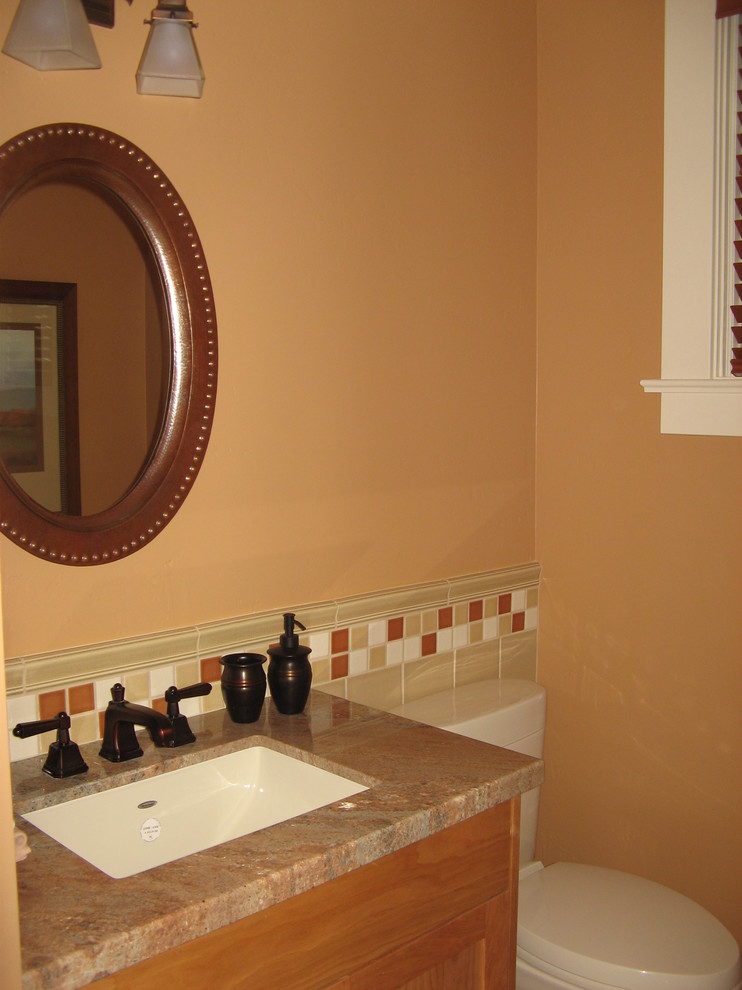 Inredning av ett amerikanskt litet toalett, med skåp i shakerstil, skåp i mellenmörkt trä, beige kakel, mellanmörkt trägolv, ett undermonterad handfat, granitbänkskiva och beige väggar