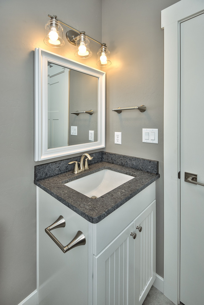 Foto på ett litet amerikanskt grå toalett, med luckor med infälld panel, vita skåp, en toalettstol med separat cisternkåpa, grå väggar, klinkergolv i keramik, ett undermonterad handfat, laminatbänkskiva och grått golv