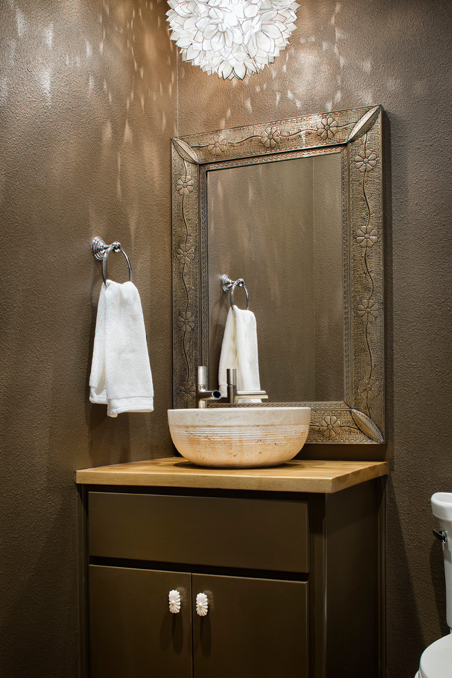 Cette image montre un WC et toilettes design en bois foncé avec une vasque, un placard à porte plane, un plan de toilette en bois et un mur marron.