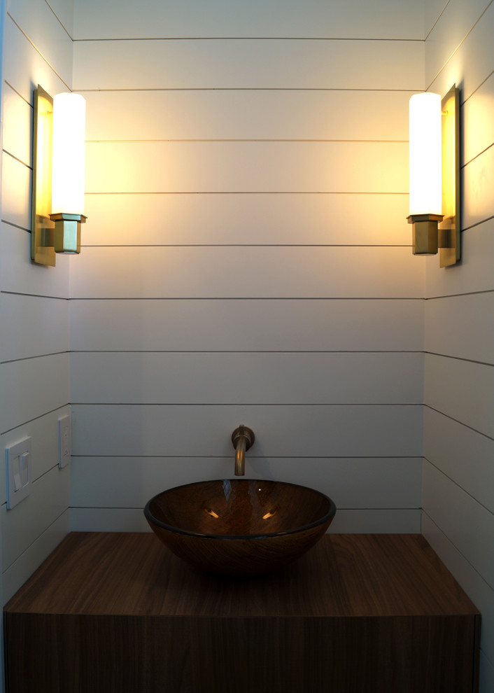 Modern inredning av ett toalett, med släta luckor, bruna skåp, en toalettstol med hel cisternkåpa, vita väggar, klinkergolv i porslin, ett fristående handfat, träbänkskiva och brunt golv