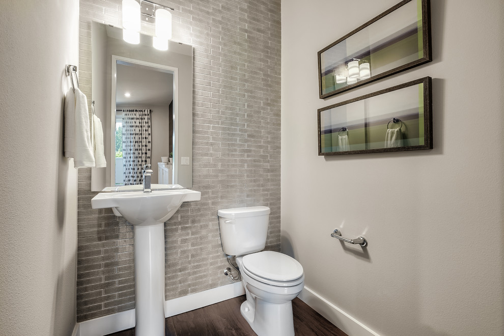 Immagine di un piccolo bagno di servizio minimalista con piastrelle grigie, piastrelle in ceramica, pareti grigie, pavimento in legno massello medio, lavabo a colonna e pavimento marrone