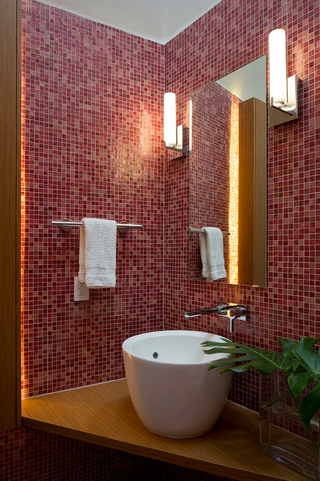 Modern inredning av ett toalett, med mosaik, ett fristående handfat, träbänkskiva och röd kakel