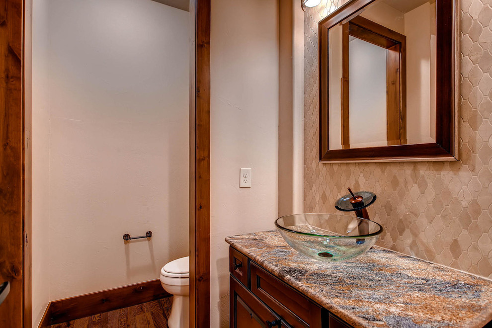 Design ideas for a large classic cloakroom in Denver with a vessel sink, raised-panel cabinets, medium wood cabinets, granite worktops, a one-piece toilet, beige tiles, stone tiles, beige walls and dark hardwood flooring.
