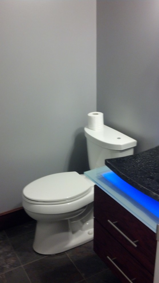 Imagen de aseo moderno pequeño con lavabo sobreencimera, encimera de vidrio, sanitario de dos piezas, baldosas y/o azulejos grises, paredes grises y suelo de pizarra