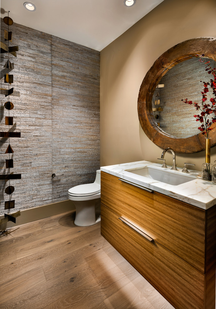 Exempel på ett stort modernt vit vitt toalett, med släta luckor, skåp i mellenmörkt trä, stenkakel, ett undermonterad handfat, bänkskiva i kvarts, en toalettstol med hel cisternkåpa, grå kakel, bruna väggar och mellanmörkt trägolv