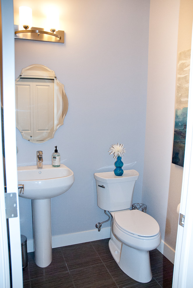 Modelo de aseo minimalista pequeño con lavabo con pedestal, sanitario de dos piezas, paredes grises y suelo de baldosas de porcelana