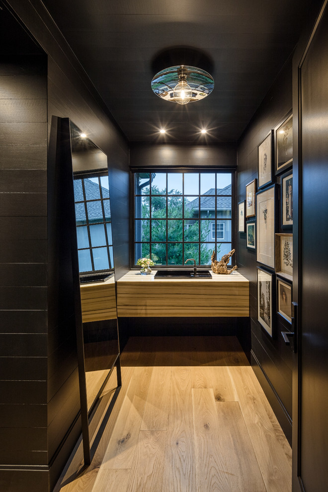 Ejemplo de aseo contemporáneo con sanitario de pared, baldosas y/o azulejos negros, paredes negras y suelo de madera clara