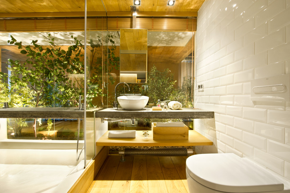 Пример оригинального дизайна: туалет среднего размера в стиле лофт с открытыми фасадами, светлыми деревянными фасадами, инсталляцией, белыми стенами, светлым паркетным полом, настольной раковиной, столешницей из бетона, белой плиткой и плиткой кабанчик