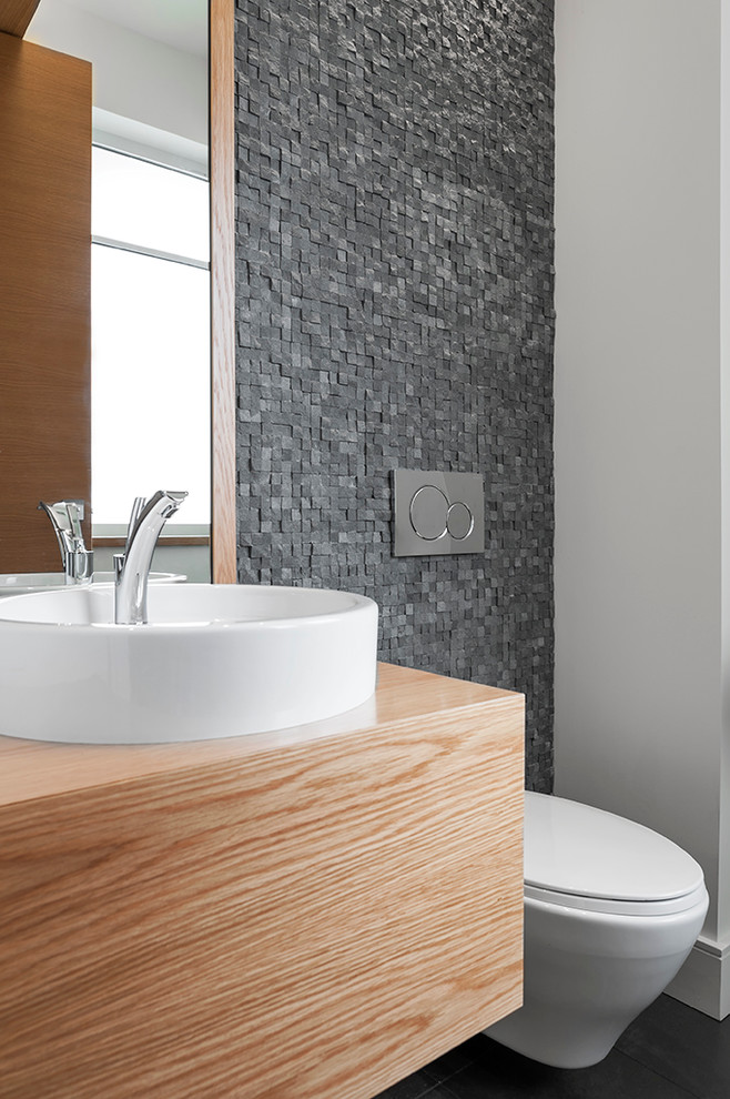 Cette image montre un WC suspendu design en bois clair de taille moyenne avec un placard à porte plane, un carrelage gris, mosaïque, un mur blanc, un sol en bois brun, une vasque, un plan de toilette en bois et un plan de toilette marron.