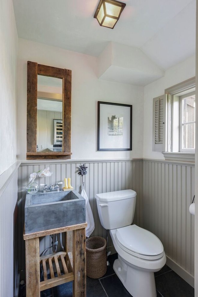 Inredning av ett lantligt toalett, med en toalettstol med separat cisternkåpa, skiffergolv och vita väggar