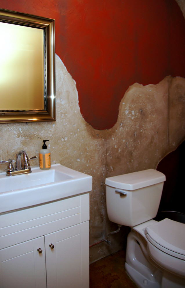 Bild på ett medelhavsstil vit vitt toalett, med släta luckor, vita skåp, en toalettstol med separat cisternkåpa, röda väggar, betonggolv, ett avlångt handfat och flerfärgat golv