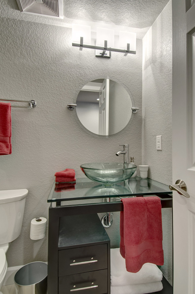 This is an example of a medium sized classic cloakroom in Denver with flat-panel cabinets, dark wood cabinets, a two-piece toilet, grey walls, porcelain flooring, a vessel sink, glass worktops and grey floors.