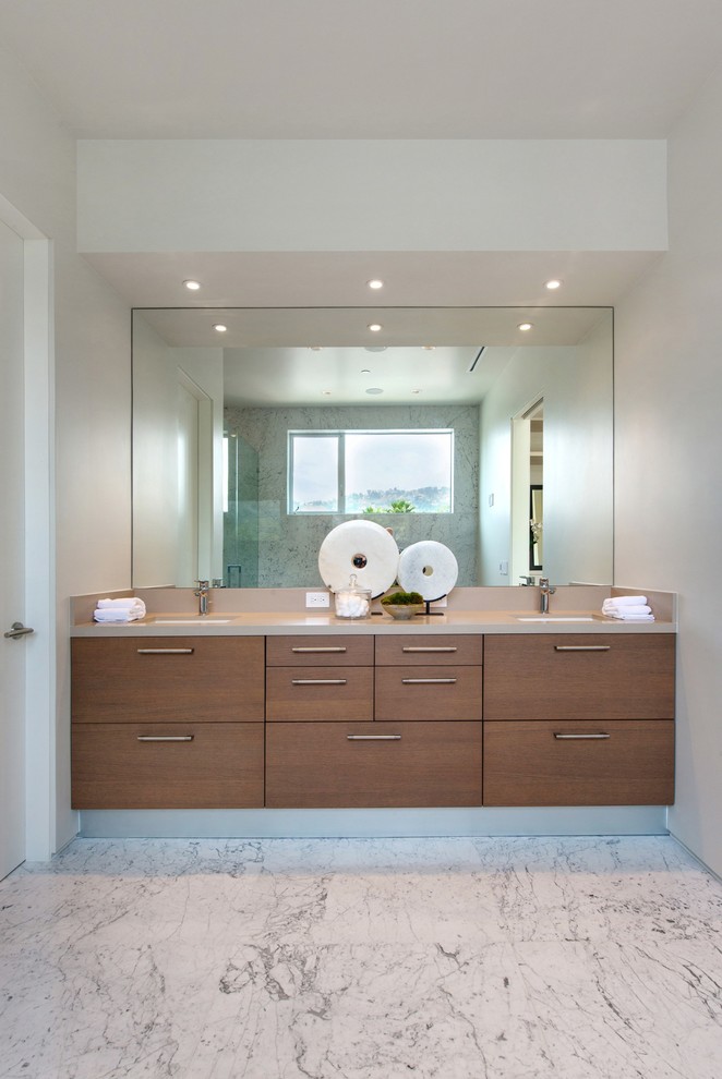 Cette photo montre un WC et toilettes moderne en bois brun de taille moyenne avec un placard à porte plane, un lavabo encastré, WC à poser, un carrelage beige, un carrelage de pierre, un mur blanc, un sol en marbre, un plan de toilette en surface solide et un sol blanc.