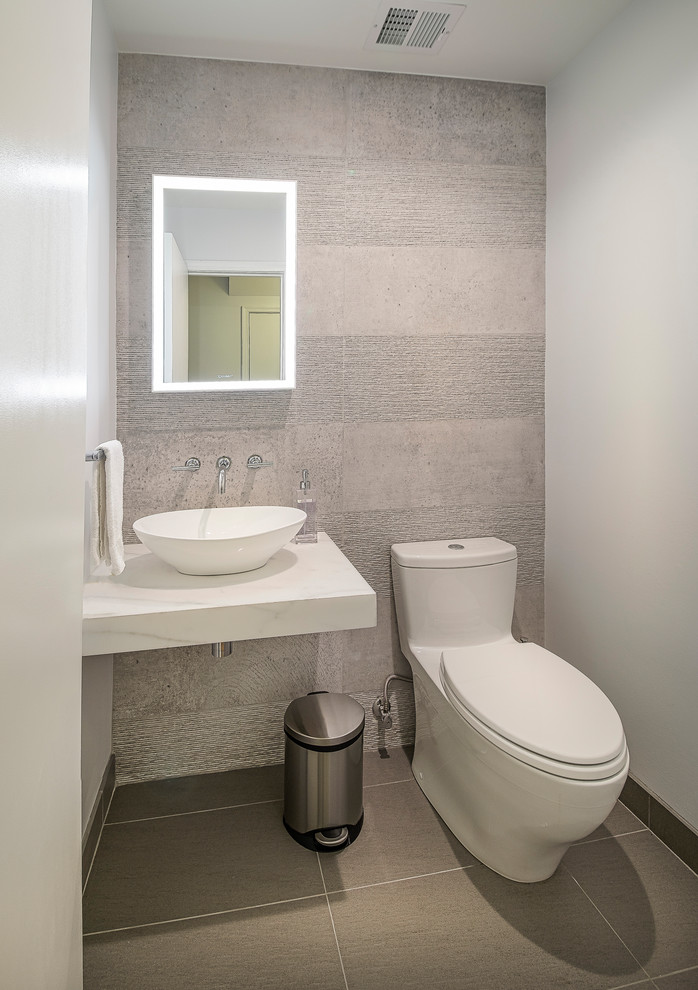 Photo of a small contemporary cloakroom in DC Metro with a one-piece toilet, beige tiles, cement tiles, beige walls, laminate floors, a vessel sink, marble worktops, beige floors and white worktops.