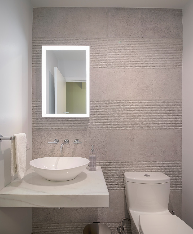 Cette image montre un petit WC et toilettes design avec WC à poser, un carrelage beige, des carreaux de béton, un mur beige, sol en stratifié, une vasque, un plan de toilette en marbre, un sol beige et un plan de toilette blanc.
