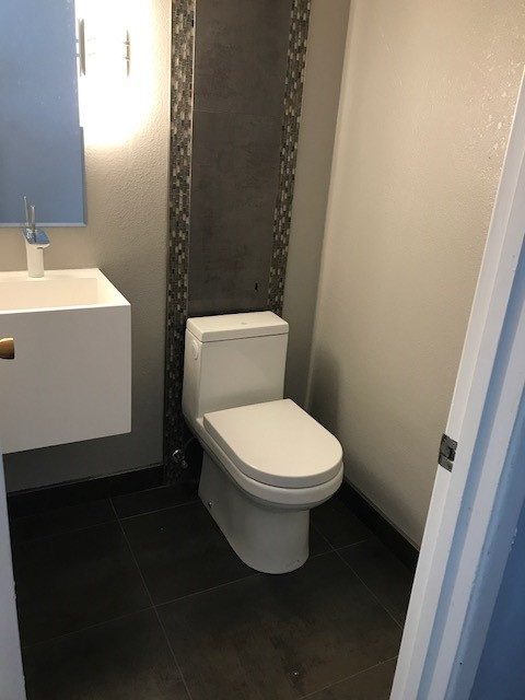 Photo of a small traditional cloakroom in San Francisco with flat-panel cabinets, white cabinets, a one-piece toilet, multi-coloured tiles, mosaic tiles, beige walls, ceramic flooring, a wall-mounted sink, solid surface worktops and black floors.