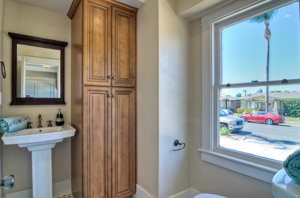 サンディエゴにあるトランジショナルスタイルのおしゃれなトイレ・洗面所 (レイズドパネル扉のキャビネット、中間色木目調キャビネット、ベージュの壁、ペデスタルシンク) の写真