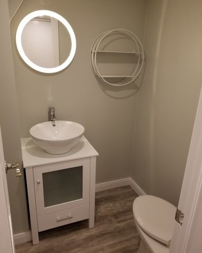 Réalisation d'un petit WC et toilettes design avec un placard en trompe-l'oeil, des portes de placard blanches, un mur gris, un sol en bois brun, une vasque, un sol marron et un plan de toilette blanc.