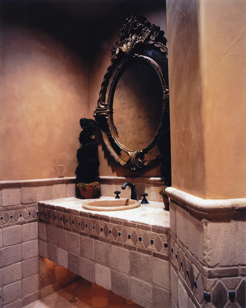Ispirazione per un bagno di servizio mediterraneo con piastrelle beige, piastrelle in pietra, pareti beige, lavabo da incasso e top piastrellato