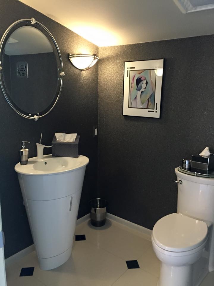 Modern inredning av ett mellanstort toalett, med släta luckor, vita skåp, en toalettstol med separat cisternkåpa, svarta väggar, klinkergolv i porslin, ett piedestal handfat, bänkskiva i akrylsten och beiget golv