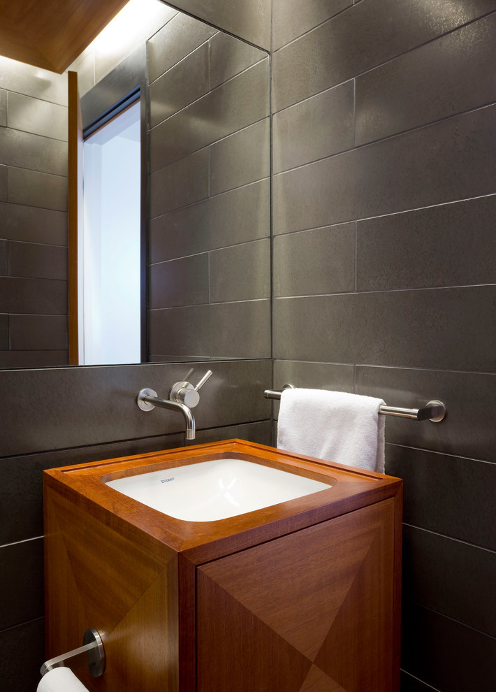 Cette image montre un WC et toilettes design en bois brun de taille moyenne avec un placard en trompe-l'oeil, un carrelage gris, un mur gris, un lavabo encastré, un plan de toilette en bois, un sol rouge, WC séparés, des carreaux de porcelaine et un sol en brique.