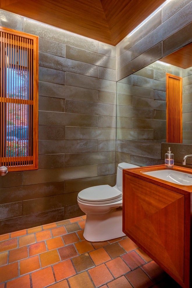 Cette photo montre un WC et toilettes tendance en bois brun de taille moyenne avec un placard en trompe-l'oeil, WC séparés, un carrelage gris, des carreaux de porcelaine, un mur gris, un sol en brique, un lavabo encastré, un plan de toilette en bois et un sol rouge.