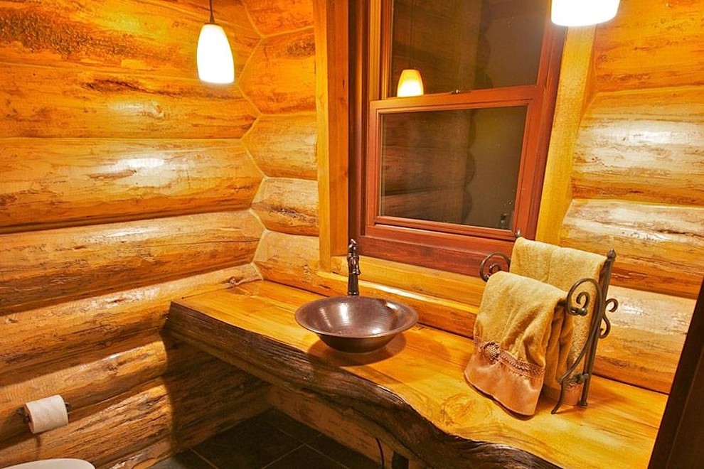 Foto på ett litet rustikt toalett, med öppna hyllor, en toalettstol med separat cisternkåpa, brun kakel, bruna väggar, skiffergolv, ett fristående handfat, träbänkskiva och grått golv