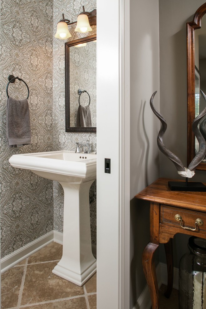 Klassisk inredning av ett litet toalett, med en toalettstol med separat cisternkåpa, brun kakel, grå väggar, travertin golv och ett piedestal handfat