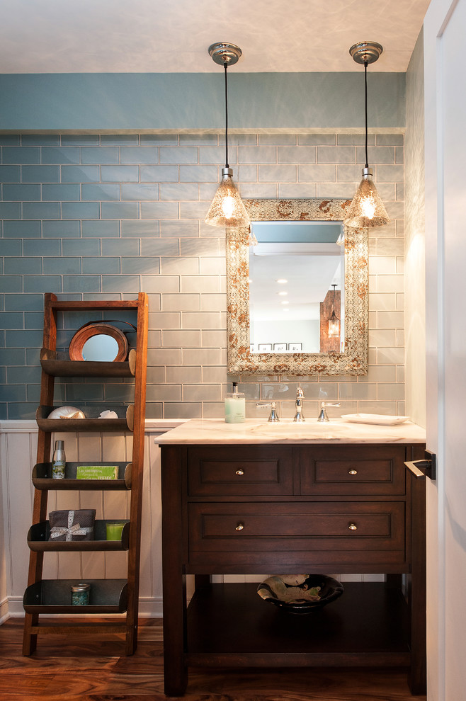 Klassisk inredning av ett mellanstort toalett, med blå väggar, mellanmörkt trägolv, ett undermonterad handfat, luckor med profilerade fronter, blå kakel, glaskakel, marmorbänkskiva, skåp i mörkt trä och brunt golv