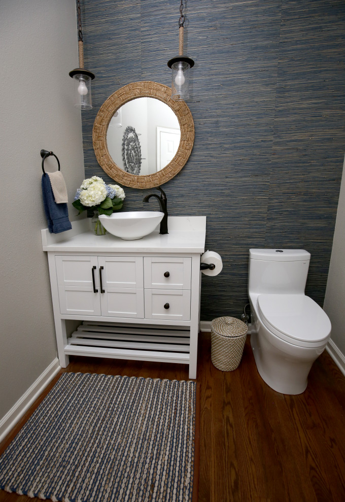 This is an example of a small beach style cloakroom in Denver with raised-panel cabinets, white cabinets, a one-piece toilet, blue tiles, blue walls, dark hardwood flooring, a vessel sink, engineered stone worktops, brown floors and white worktops.