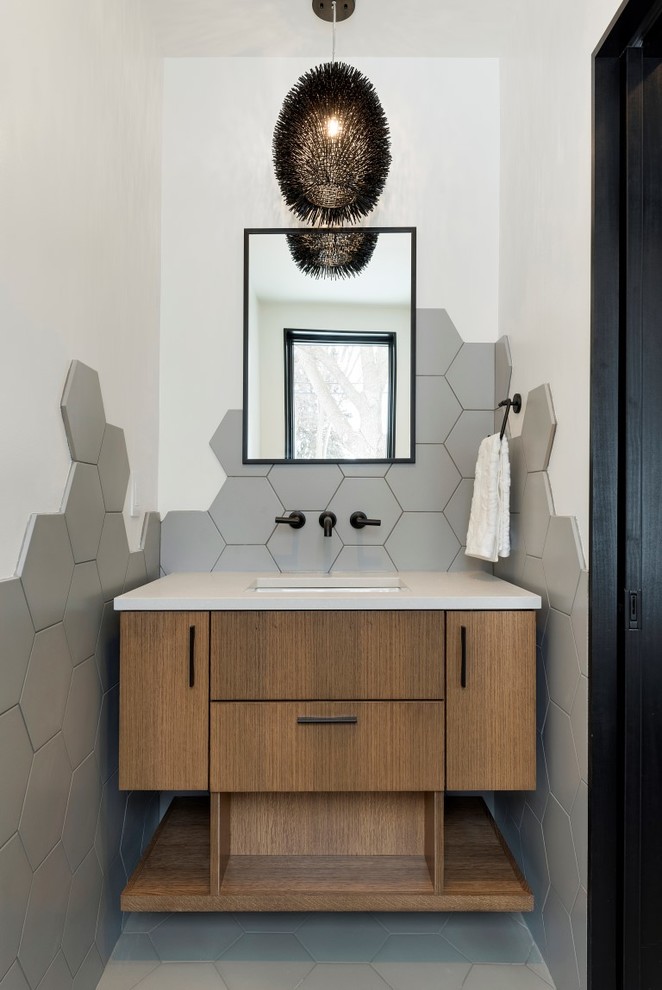 Bild på ett funkis grå grått toalett, med släta luckor, skåp i mellenmörkt trä, grå kakel, grå väggar, ett undermonterad handfat och grått golv