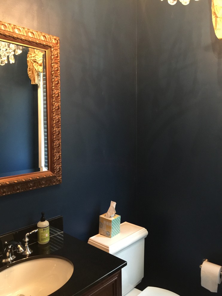 Example of a small trendy powder room design in Cleveland with recessed-panel cabinets, dark wood cabinets, a two-piece toilet, blue walls, an undermount sink, solid surface countertops and black countertops
