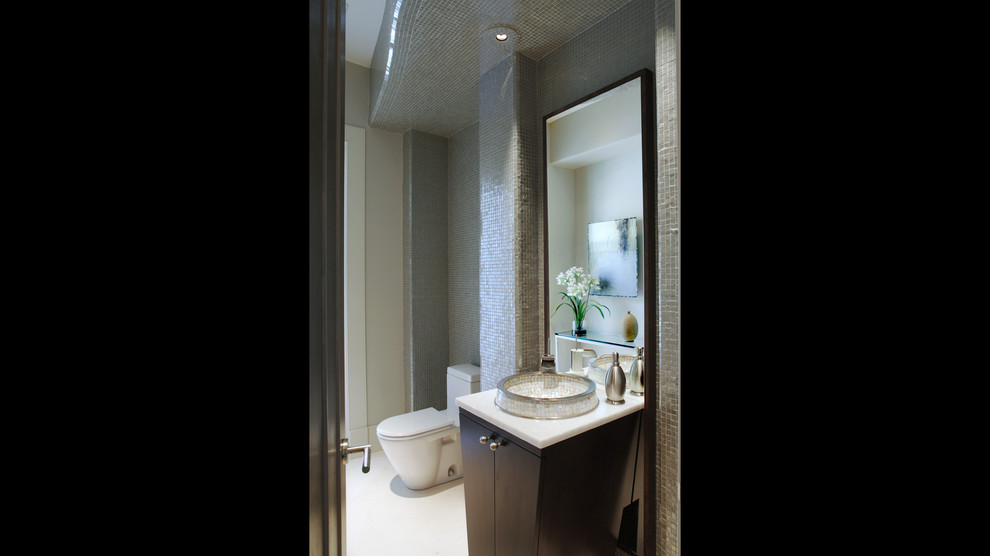 Modern inredning av ett toalett, med marmorbänkskiva, en toalettstol med hel cisternkåpa, grå kakel, mosaik och klinkergolv i keramik