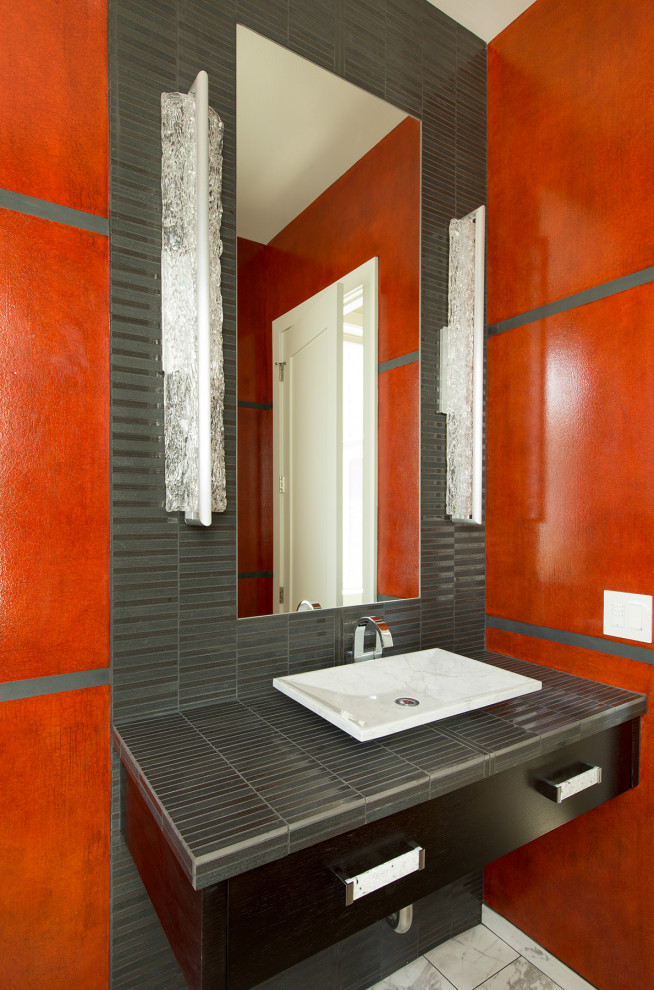 Bild på ett stort funkis grå grått toalett, med släta luckor, svarta skåp, en toalettstol med hel cisternkåpa, röd kakel, mosaik, röda väggar, klinkergolv i porslin, ett fristående handfat, kaklad bänkskiva och vitt golv