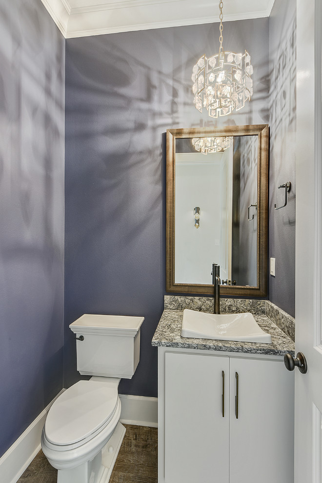 Inredning av ett klassiskt mellanstort grå grått toalett, med släta luckor, vita skåp, en toalettstol med separat cisternkåpa, lila väggar, mörkt trägolv, ett nedsänkt handfat, granitbänkskiva och brunt golv