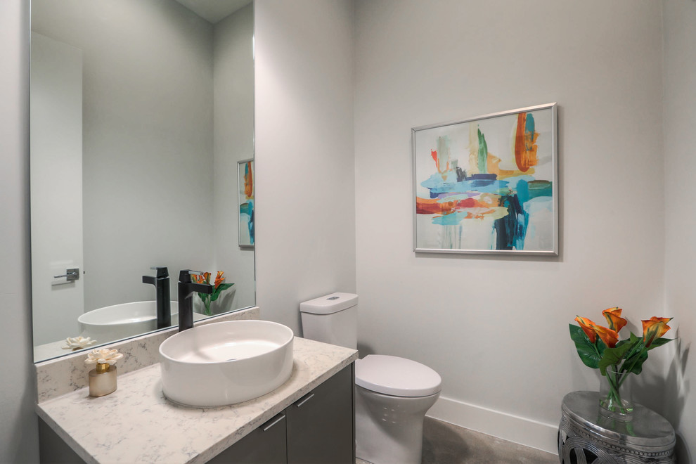 Moderne Gästetoilette mit flächenbündigen Schrankfronten, grauen Schränken, Wandtoilette mit Spülkasten, weißer Wandfarbe, Betonboden, Aufsatzwaschbecken, Quarzwerkstein-Waschtisch, grauem Boden und weißer Waschtischplatte in Houston