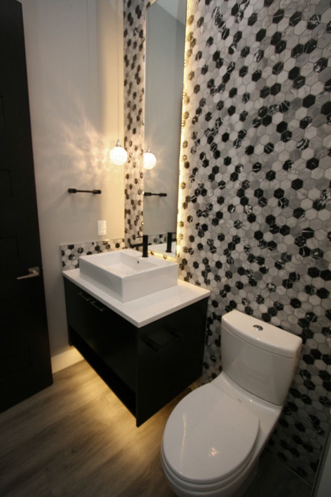 Idée de décoration pour un WC et toilettes design de taille moyenne avec un placard à porte plane, des portes de placard noires, WC à poser, un carrelage noir et blanc, un carrelage de pierre, un mur gris, un sol en vinyl, une vasque, un plan de toilette en quartz modifié, un sol gris et un plan de toilette blanc.